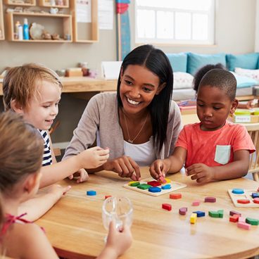 Teacher And Pupils Using Wooden Shapes In Montessori School